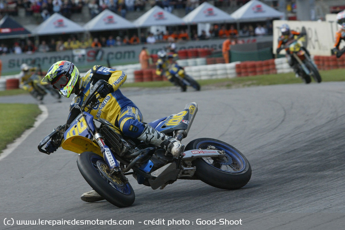 Pilote de supermotard en glisse dans un virage sur circuit, pied tendu vers l'intérieur