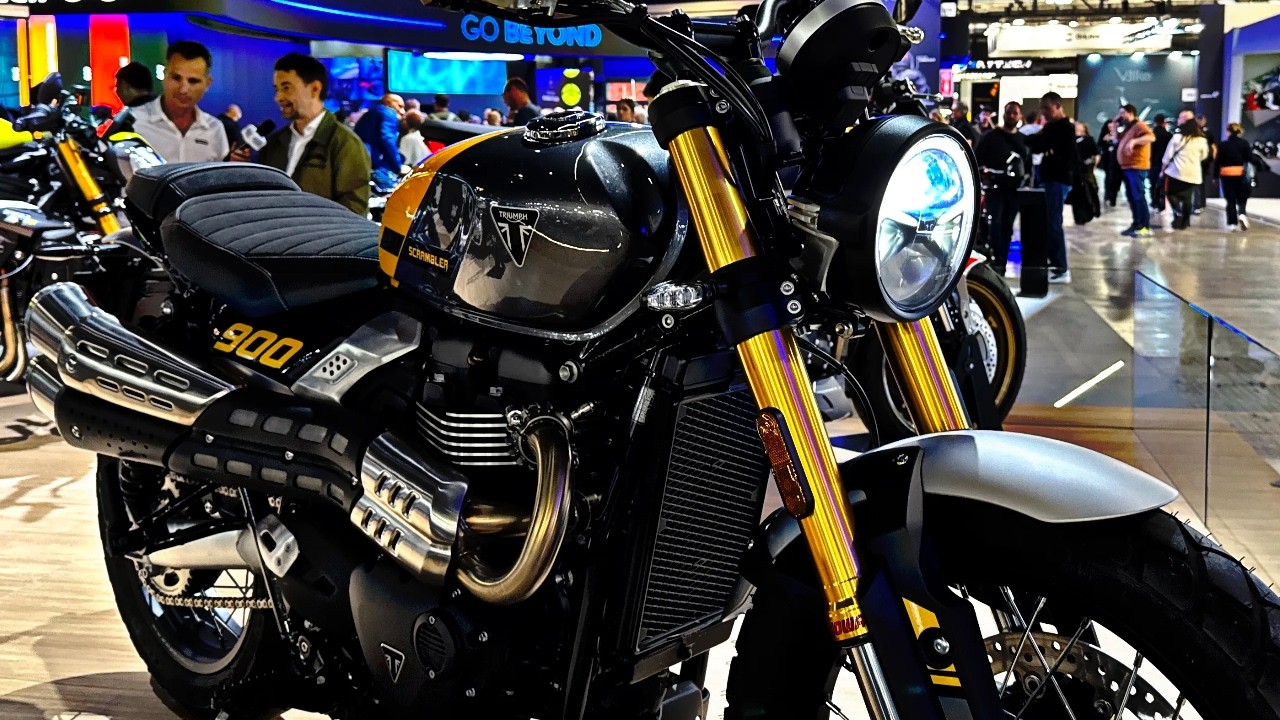 Scrambler rétro posé sur une route de campagne, guidon large et pneus mixtes